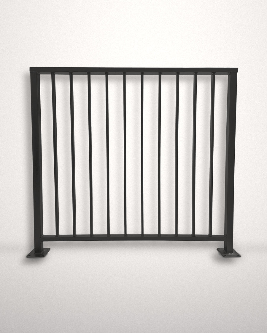Axis vertical bar railing panel in matte black powder coated steel standing against a plain wall — custom welded guardrail with flat top cap rail and bolt-down base plates, made to size in New Jersey