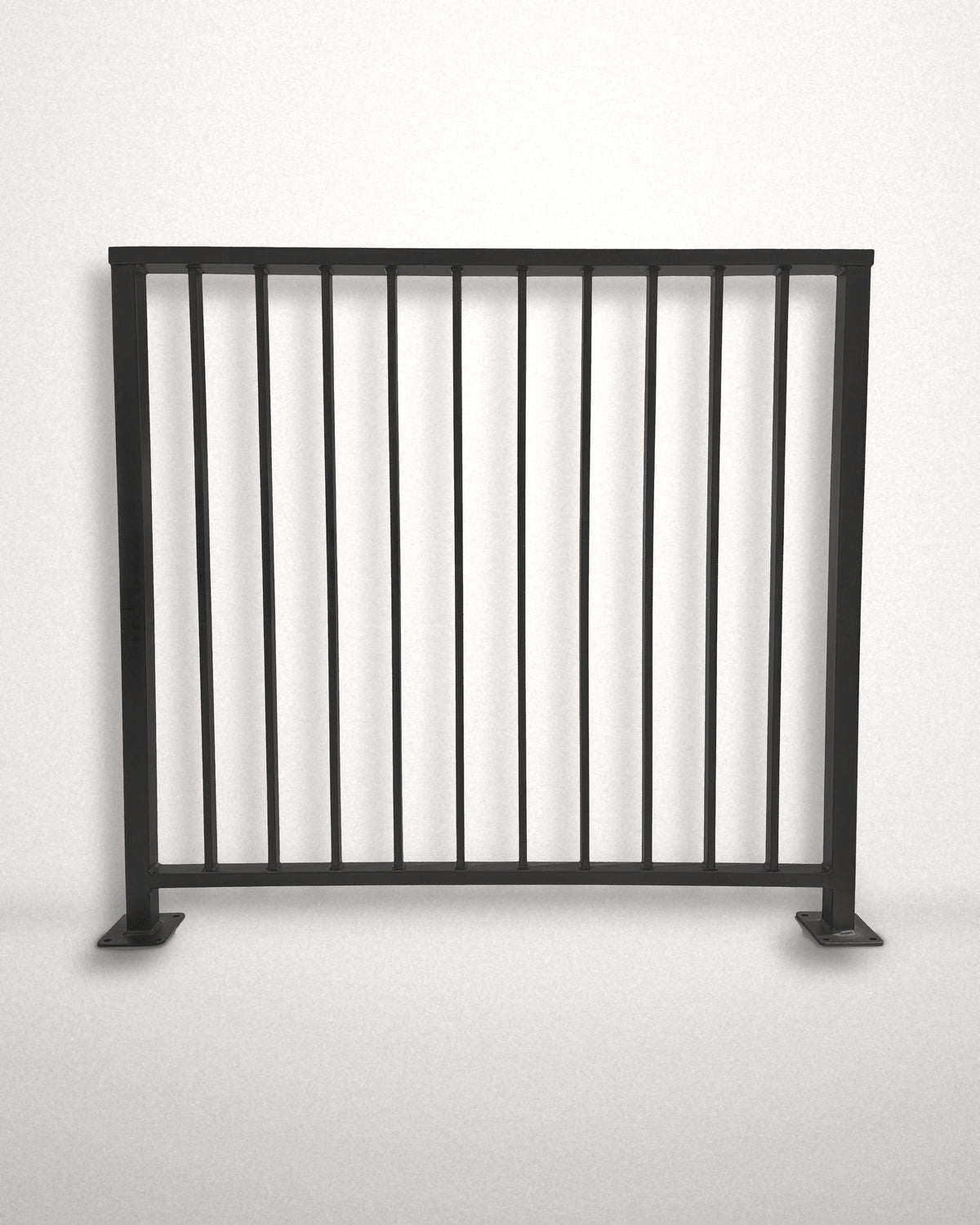 Axis vertical bar railing panel in matte black powder coated steel standing against a plain wall — custom welded guardrail with flat top cap rail and bolt-down base plates, made to size in New Jersey