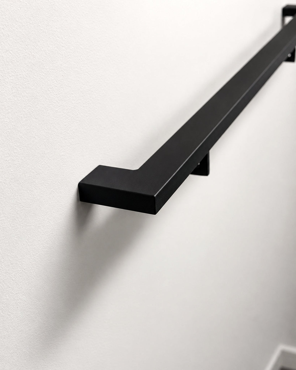2 inch by 1 inch matte black steel handrail mounted on a wall, showing the mitred return end and wall bracket