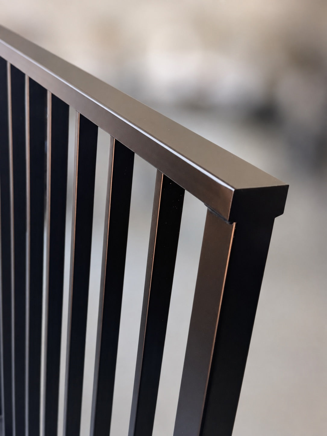 Close-up of a Barzel Axis railing — matte black powder coated steel cap rail meeting the corner post, showing the mitred joint and evenly spaced vertical bars