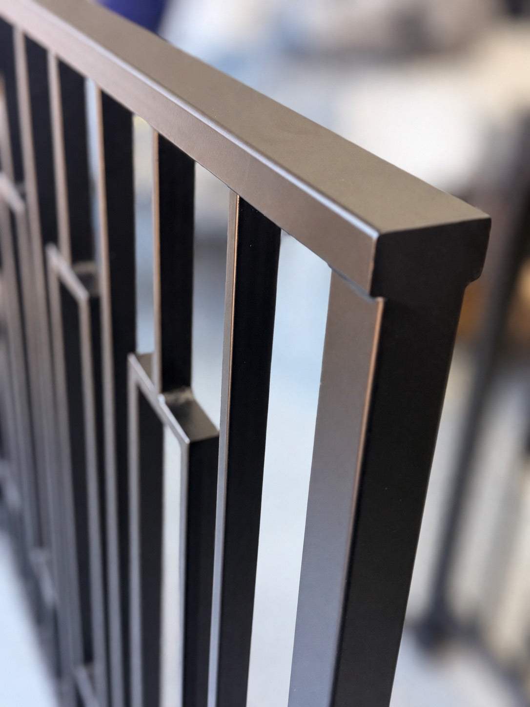 Close-up of a Barzel Axis railing corner — matte black powder coated steel cap rail mitred over the corner post, with evenly spaced vertical bars behind
