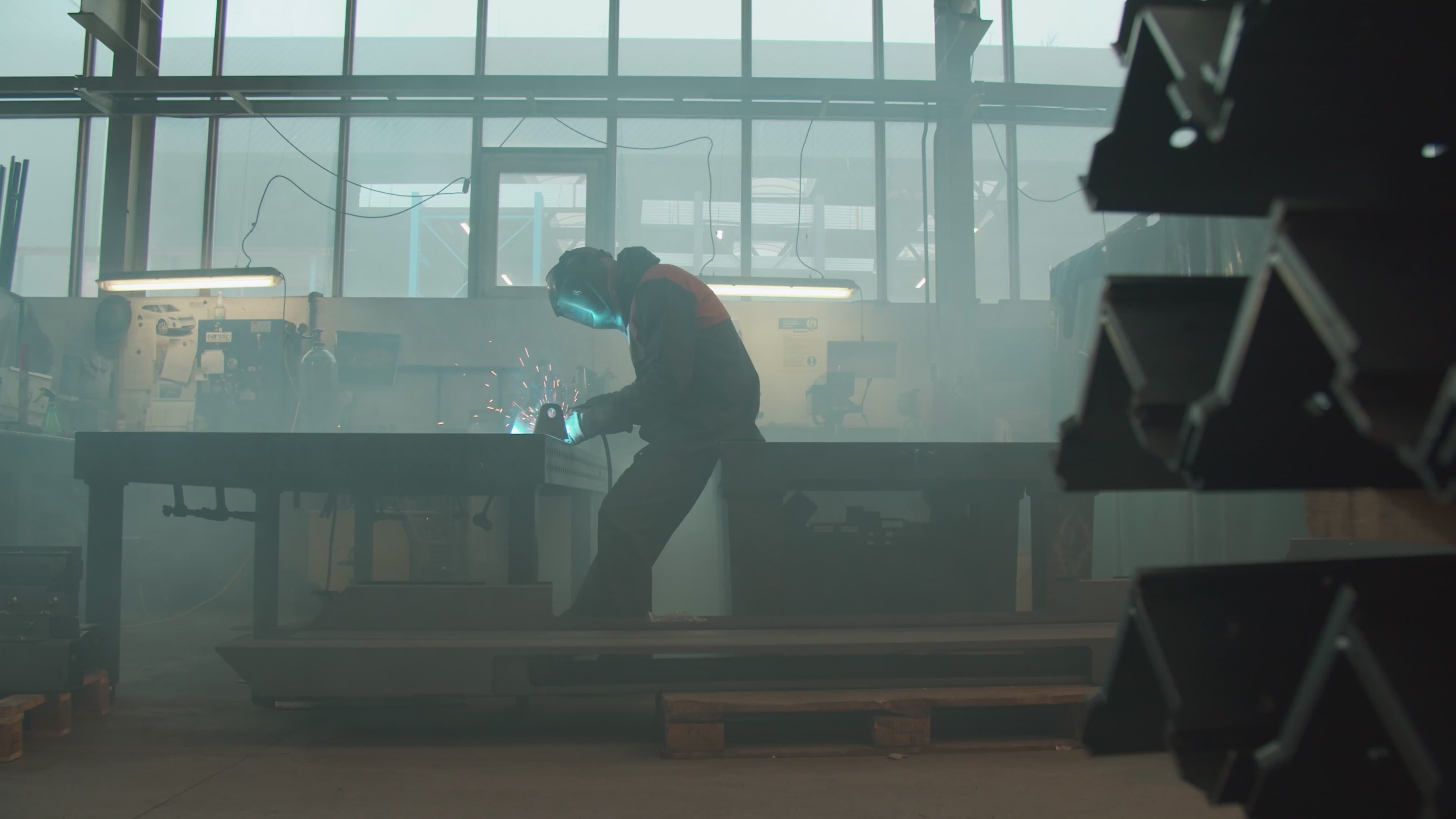 Welder working at a distance in the fabrication shop, warm sparks flying